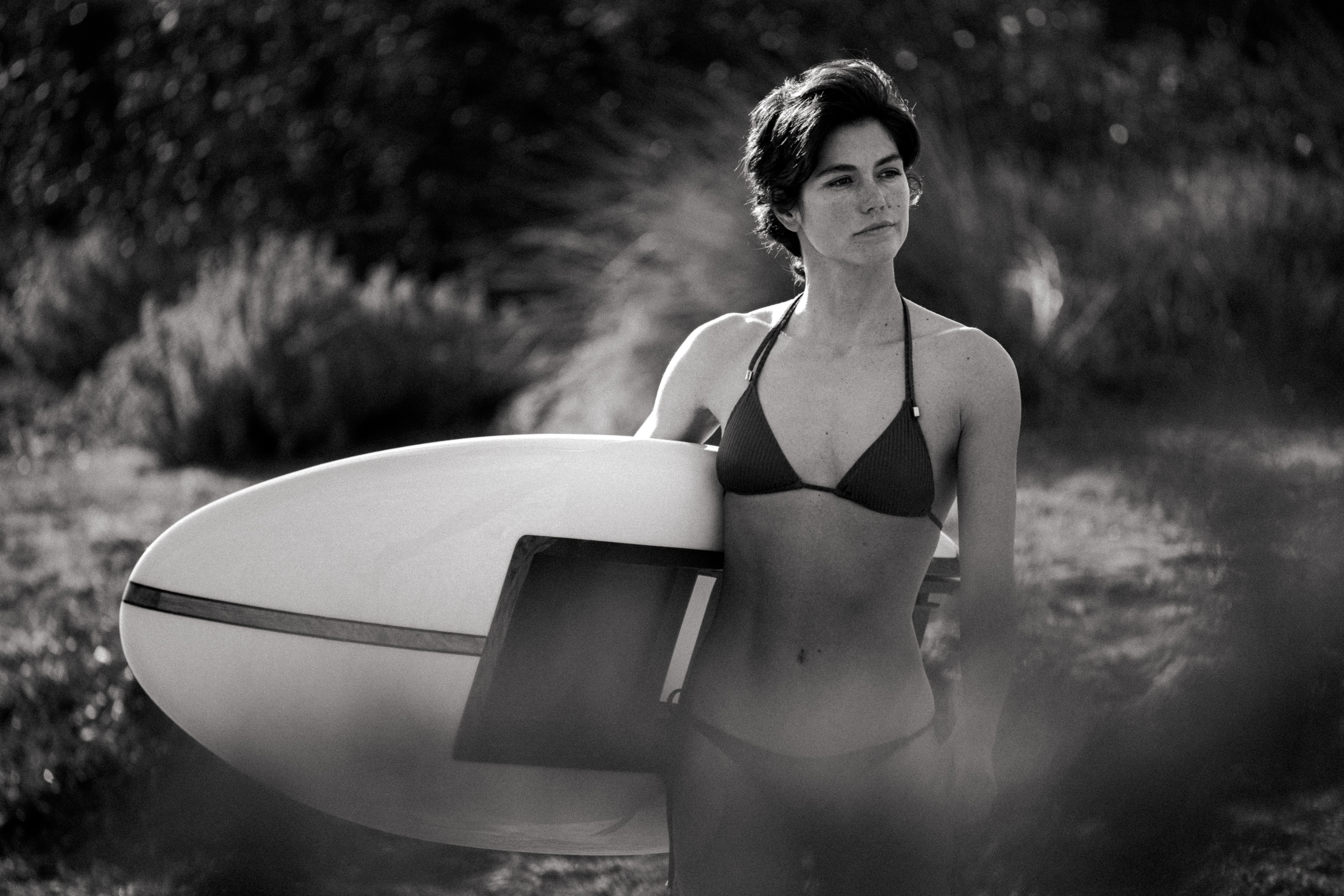 Frau im Bikini, die ein LIND Surfbrett in einer natürlichen Umgebung hält.