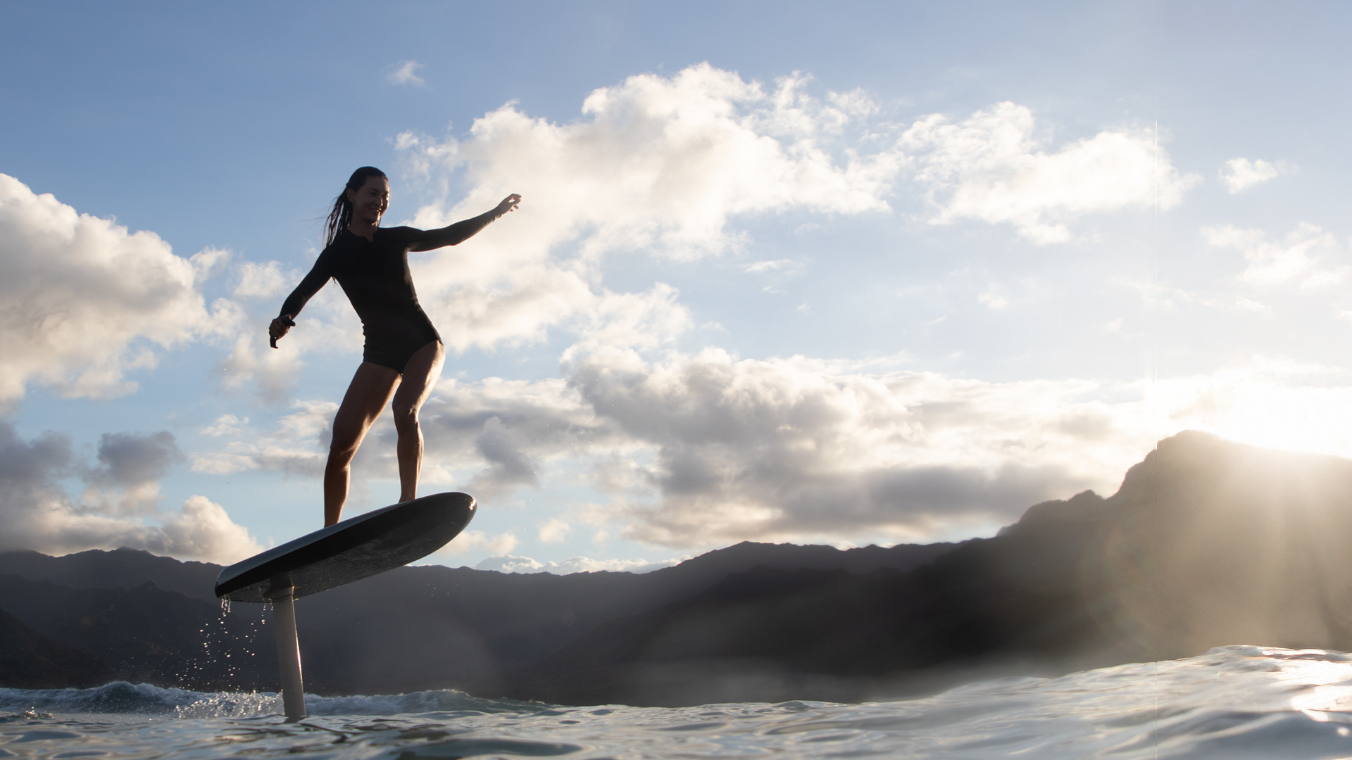 Eine Frau in einem Neoprenanzug lächelt, während sie auf einem Fliteboard auf dem Meer foilt.