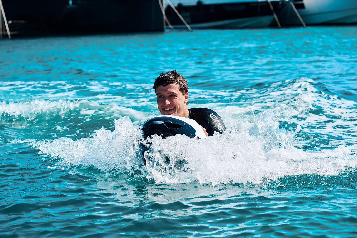 Ein Mann lächelt in die Kamera, während er auf Mallorca mit einem weißen Seabob auf dem Meer fährt.