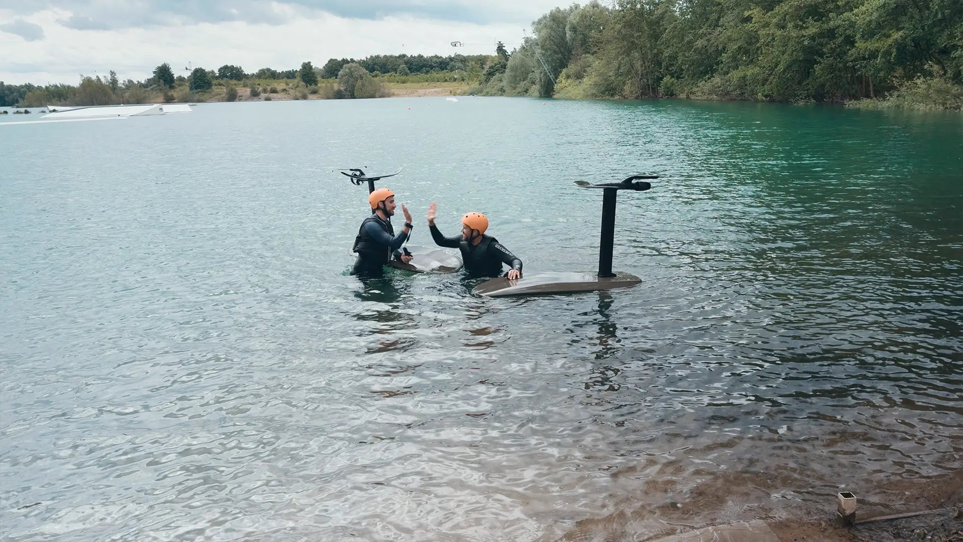 Zwei Personen in Neoprenanzügen mit Fliteboards im Wasser auf einem See.