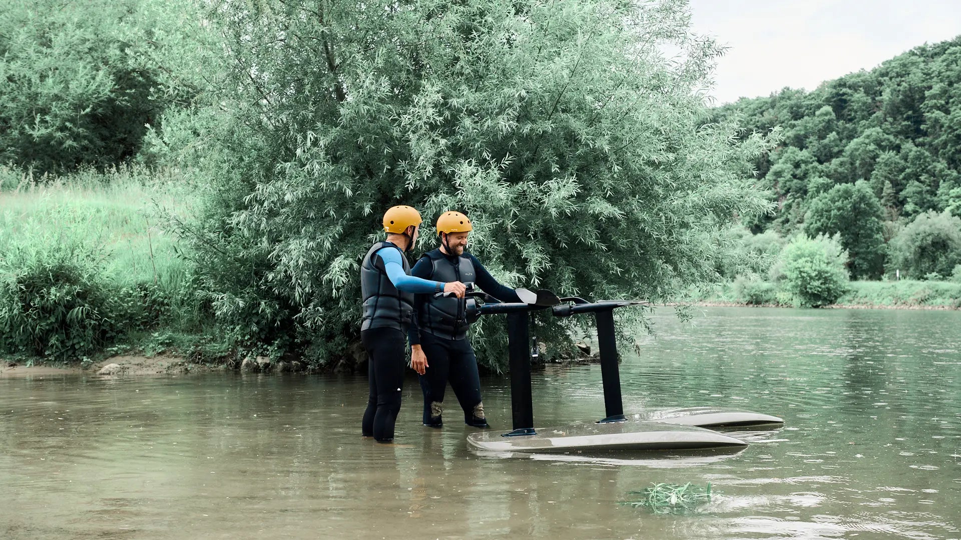 Zwei Männer stehen bis zu den Knien im Fluss und halten die Wings ihrer Fliteboards.