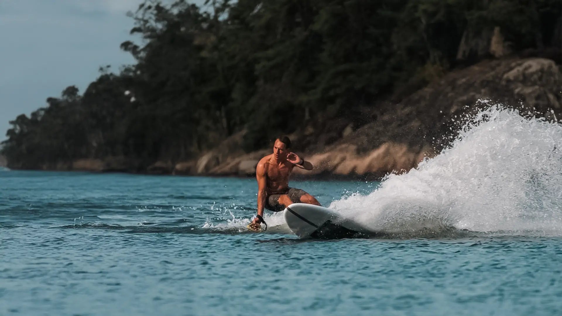 Ein Mann in Badeshorts surft dynamisch auf dem Meer mit dem Lind Surfboard.