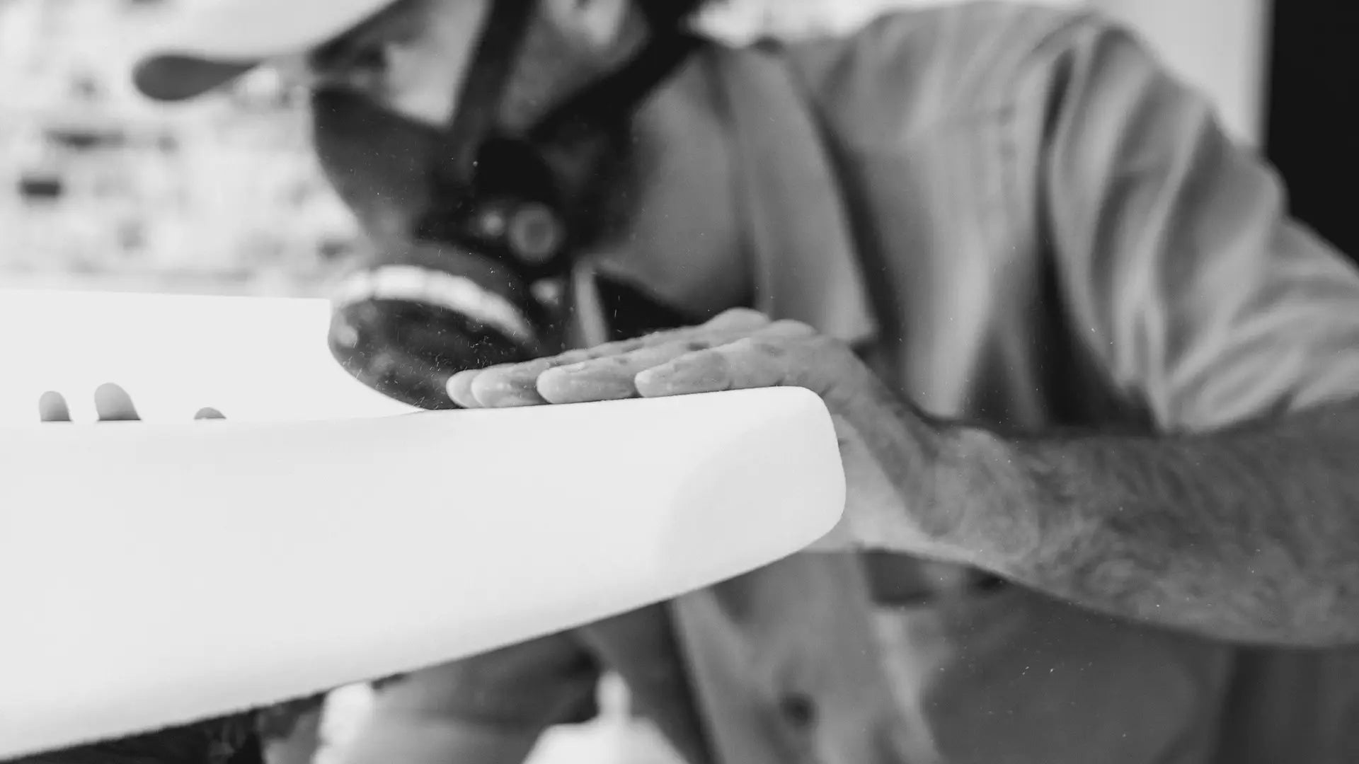 Ein Schwarzweißbild eines Mannes mit einer Schutzmaske, der ein Lind Surfboard hält.