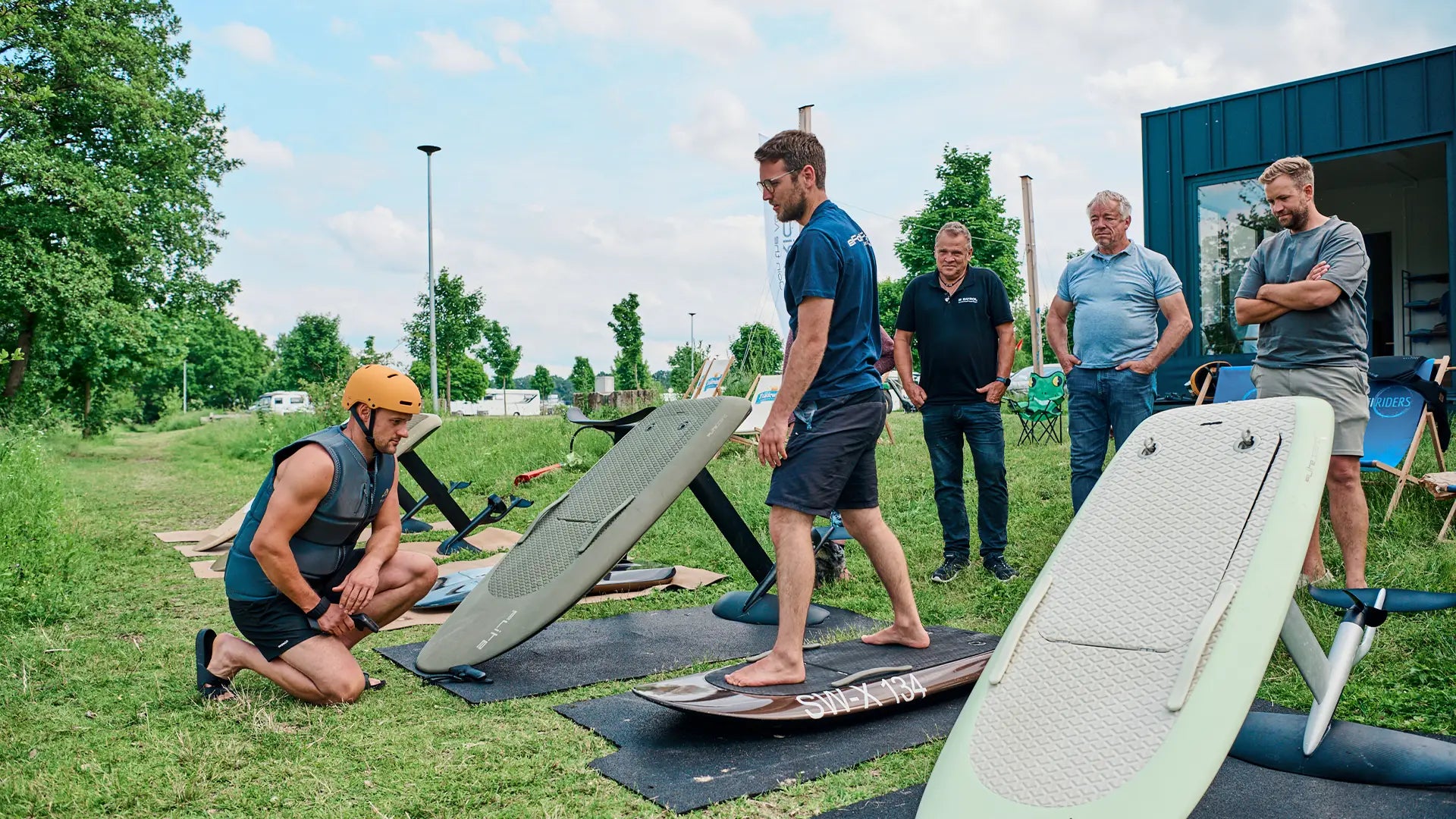 Ein eFoil-Lehrer steht auf einem Fliteboard und erklärt einer Gruppe von Leuten, wie es funktioniert.