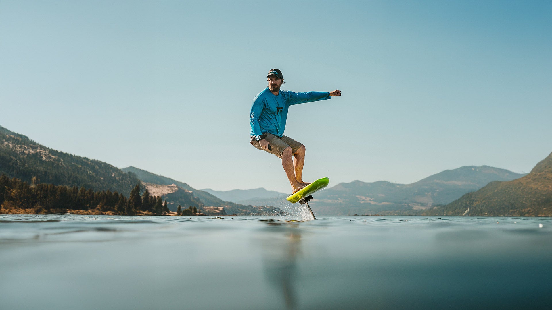 Ein Mann fährt auf dem Wasser inmitten der Natur mit einem Foil, an dem ein Foil Drive befestigt ist.