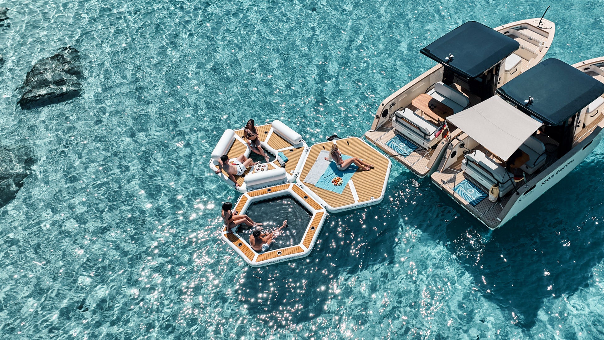 Aus der Vogelperspektive sieht man zwei Motorboote auf dem Meer, an denen die Yachtbeach befestigt sind und auf denen Menschen sitzen.
