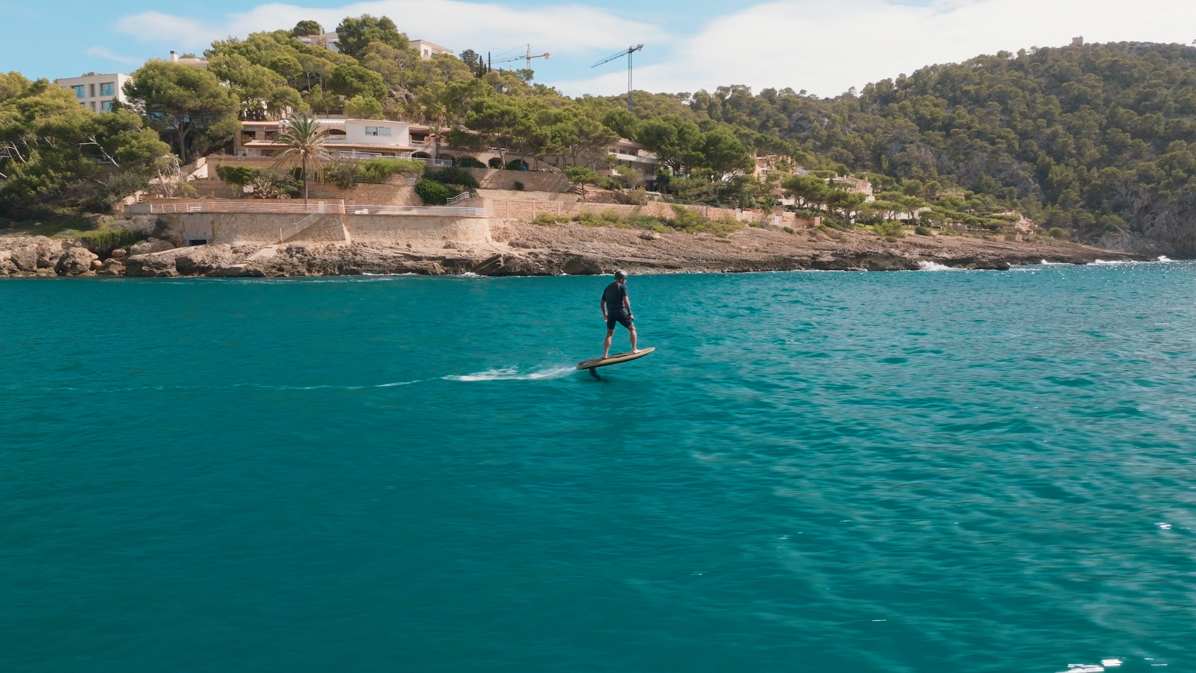 Eine Person efoilt auf einem Fliteboard auf dem Meer, mit mediterranen Bergen im Hintergrund.
