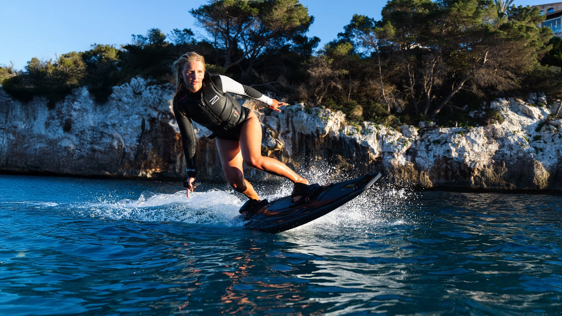 Person Awake Boarding auf einem Gewässer mit felsigen Klippen und Bäumen im Hintergrund