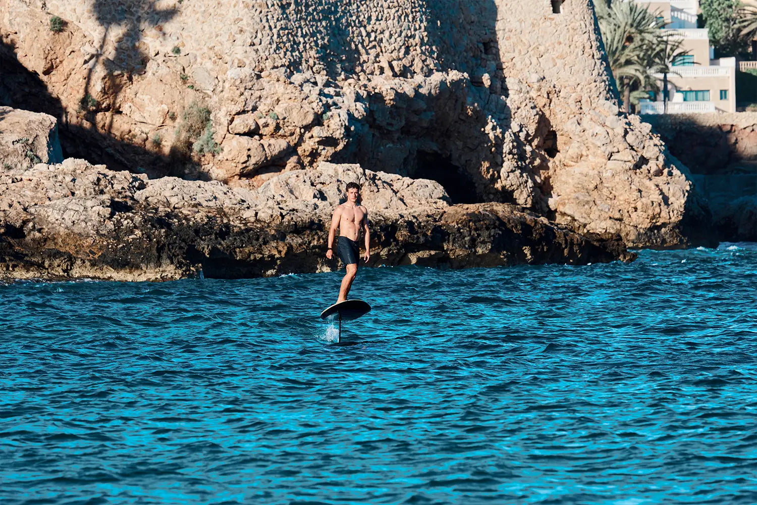Ein Junge eifert auf einem fliteboard am Meer in Mallorca, im Hintergrund sind braune Felsen zu sehen.