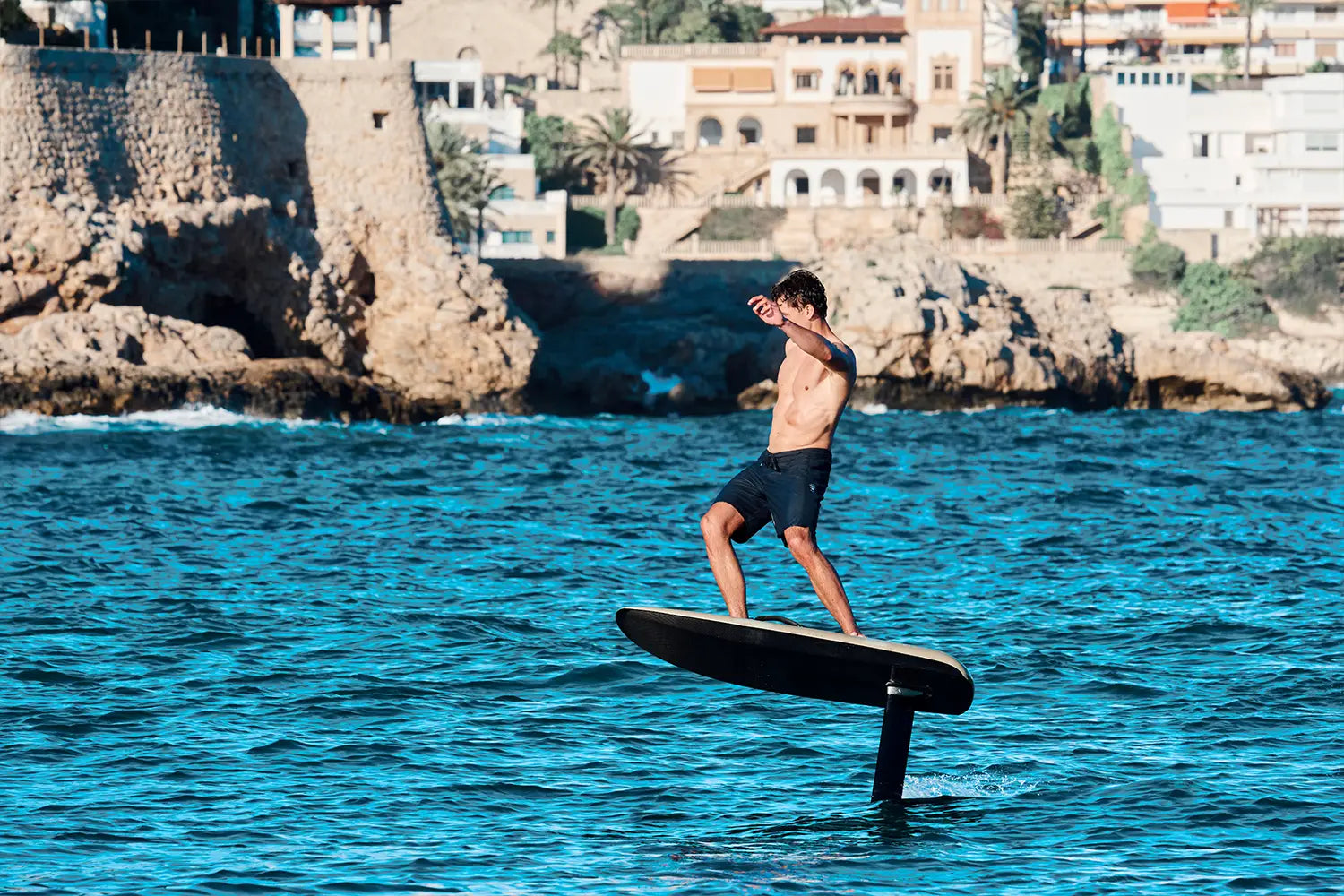 Ein Junge eifert auf einem fliteboard am Meer in Mallorca, im Hintergrund sind braune Felsen zu sehen.