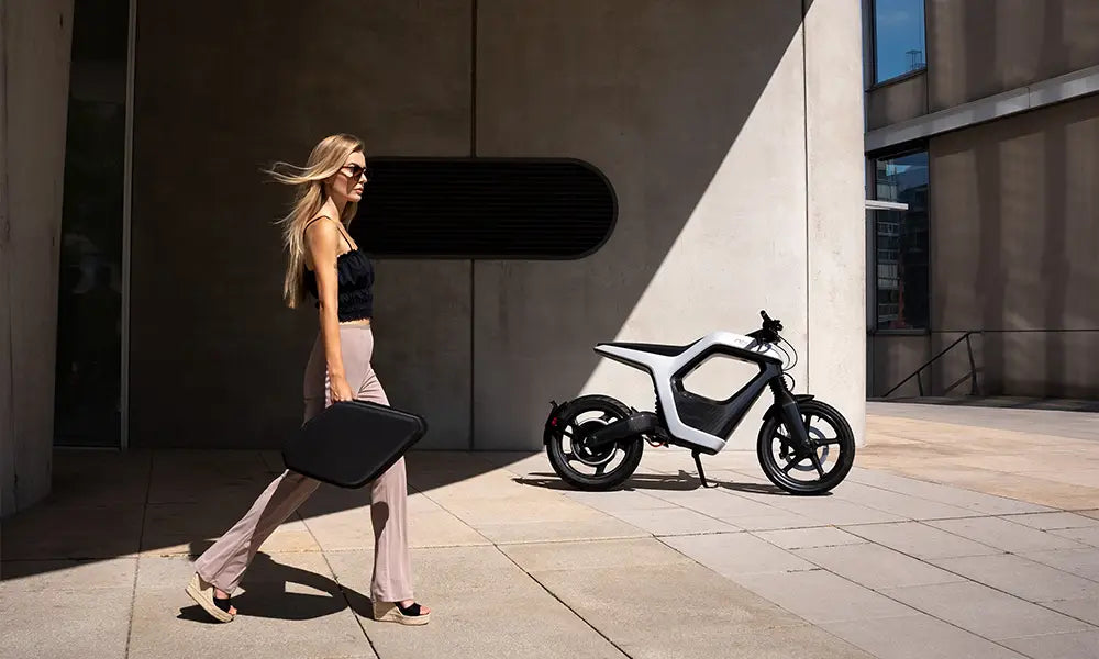 Eine Frau geht mit einer stylischen Tasche die Straße entlang, im Hintergrund ein weißes Novus Bike.
