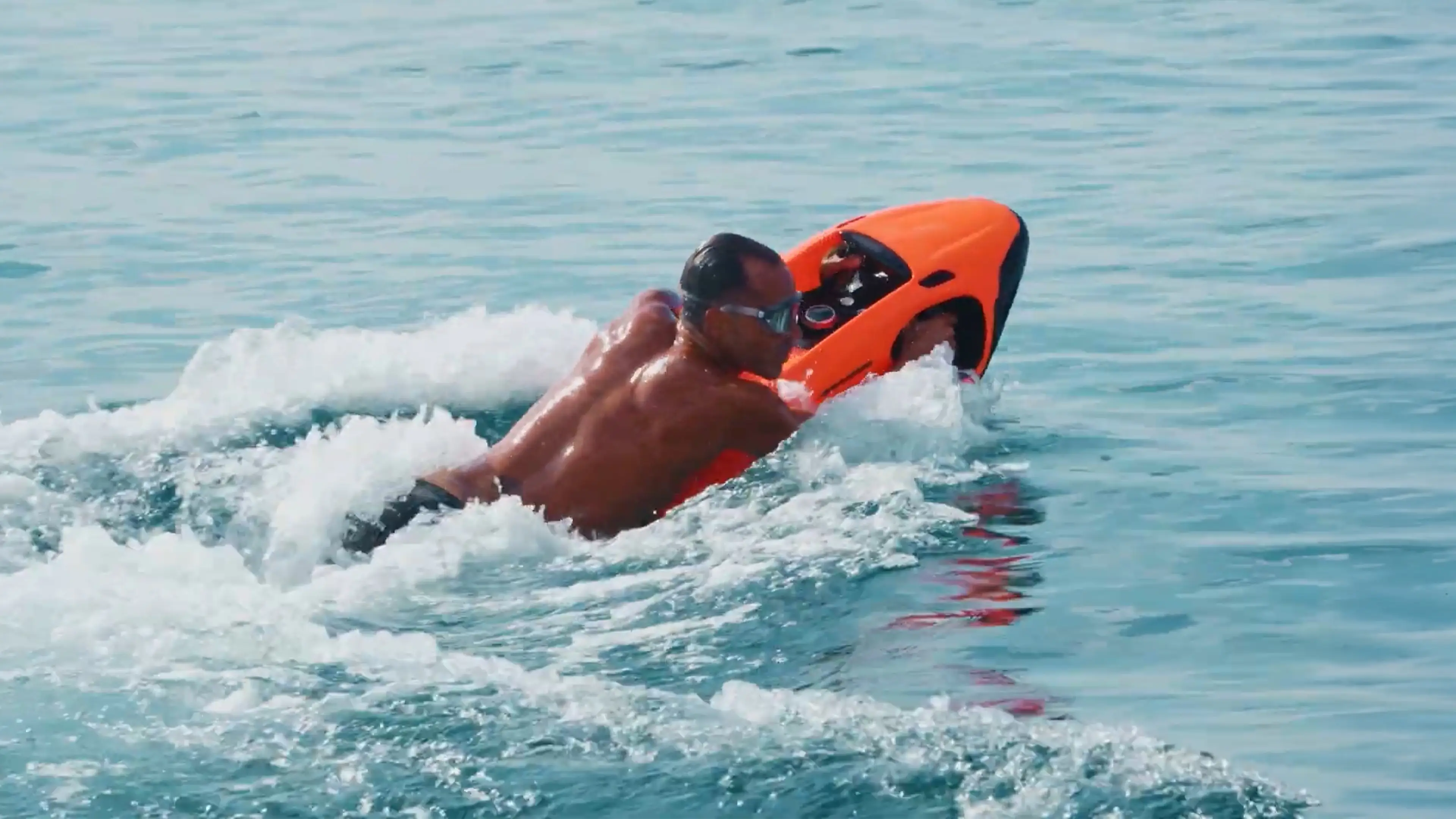Ein Mann trägt eine Taucherbrille und fährt mit einem orangefarbenen Seabob auf dem Meer.