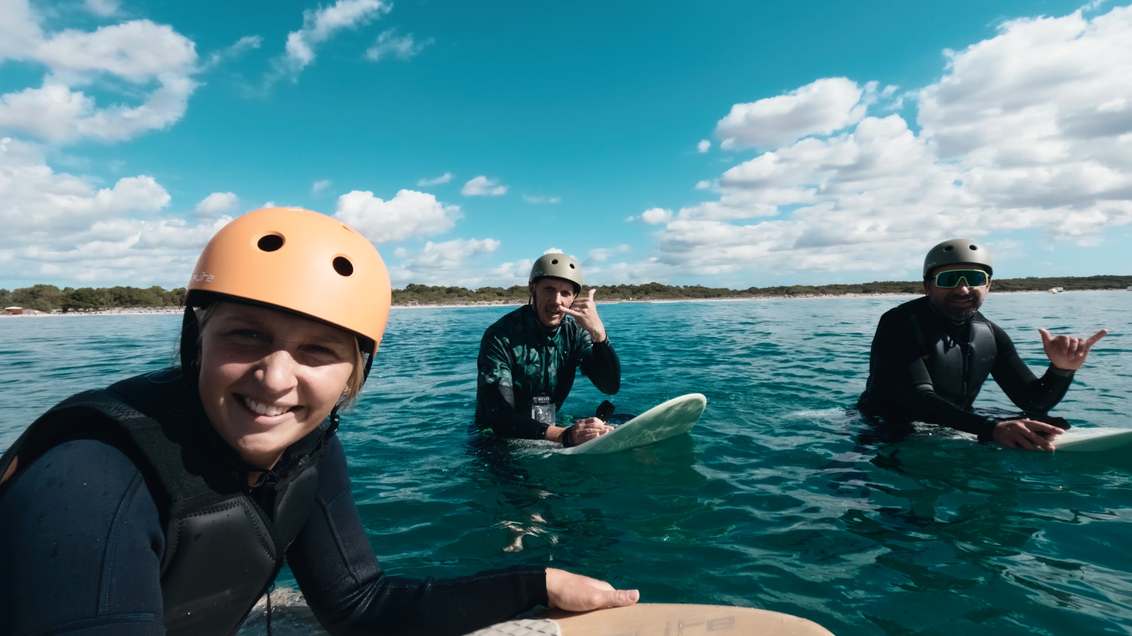 Drei Personen sitzen auf dem Meer auf ihren Fliteboards in Neoprenanzügen und Flite-Helmen und lächeln in die Kamera.