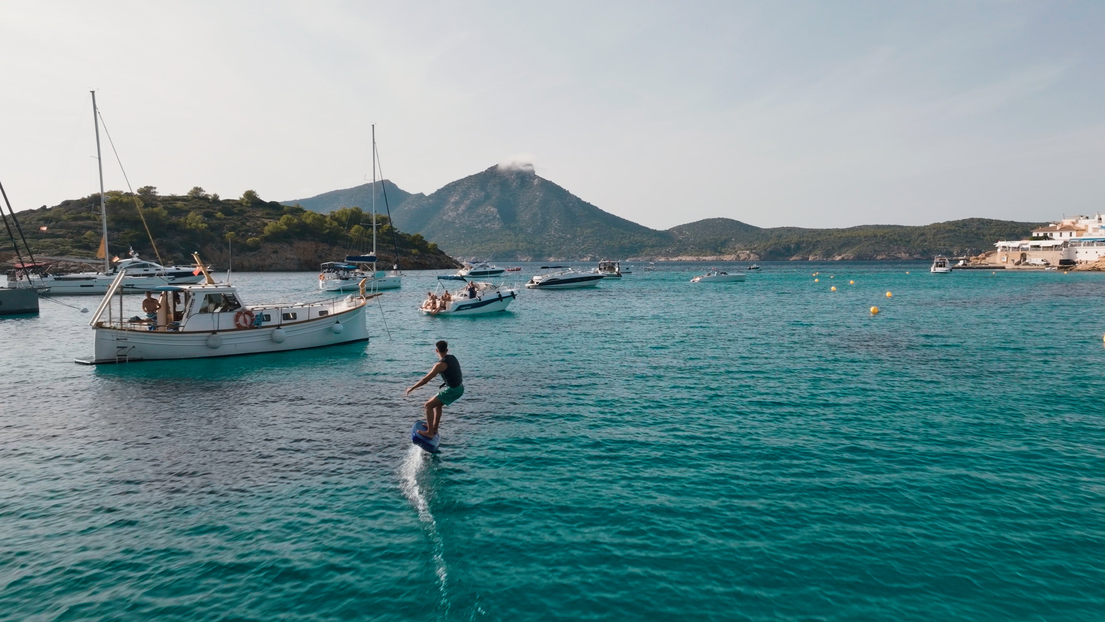 Ein Mensch fährt auf seinem fliteboard auf dem Meer zwischen Booten umher.
